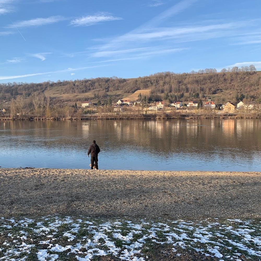 A man stands on a snowy riverbank looking out at a calm river.